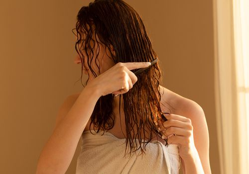Woman combing her wet hair in her bathroom.